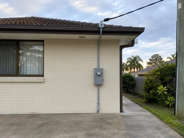 Exterior brick house wall with overhead service cable and meter box under the eaves in Charmhaven