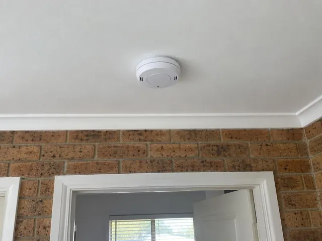 Ceiling smoke alarm above a brick wall and doorway in a home interior in Lake Haven